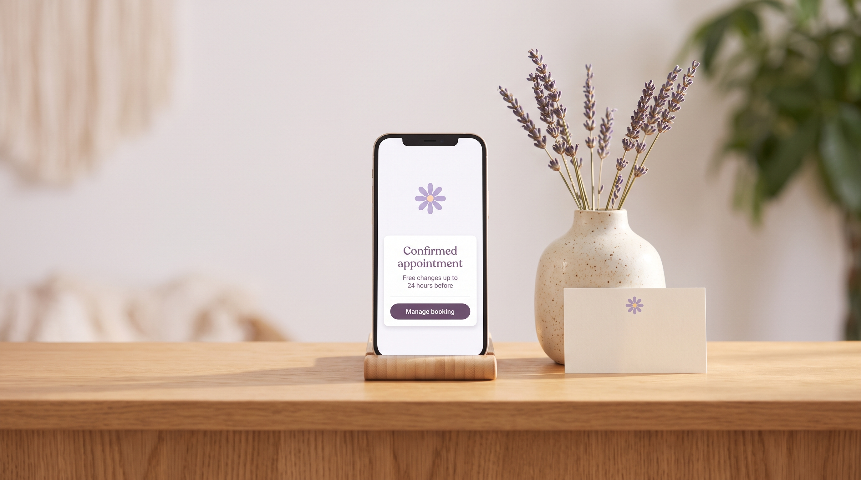 A smartphone on a wooden reception desk showing a confirmed appointment with free changes up to 24 hours before and a Manage booking button, beside a vase of lavender